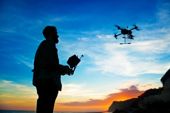 Pilote tenant sa radiocommande, avec un drone en vol devant lui